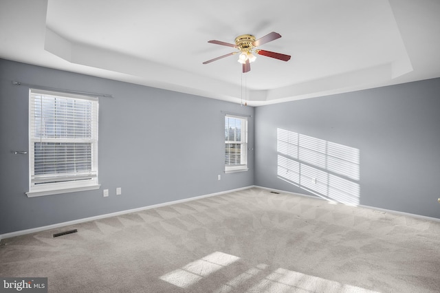 empty room featuring carpet floors, a raised ceiling, and ceiling fan