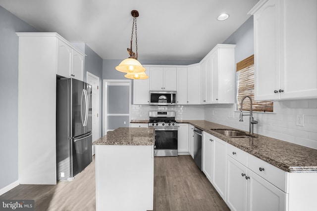 kitchen featuring sink, appliances with stainless steel finishes, hanging light fixtures, a kitchen island, and dark stone counters