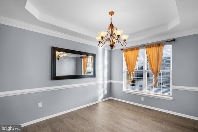 unfurnished room featuring a raised ceiling, wood-type flooring, and an inviting chandelier