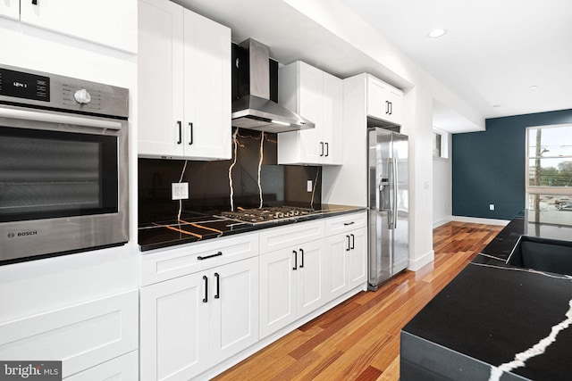 kitchen featuring white cabinets, backsplash, light hardwood / wood-style floors, stainless steel appliances, and wall chimney exhaust hood