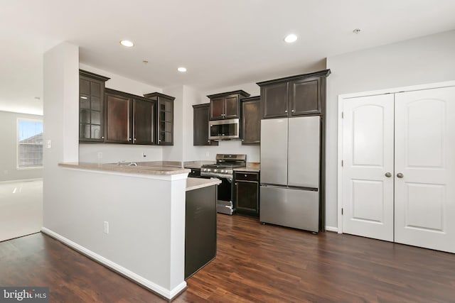 kitchen with a peninsula, light countertops, appliances with stainless steel finishes, dark brown cabinets, and glass insert cabinets