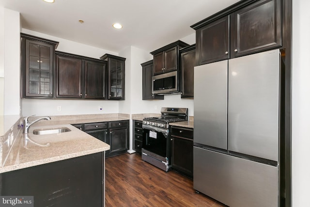 kitchen with stainless steel appliances, dark wood-type flooring, a sink, dark brown cabinets, and glass insert cabinets