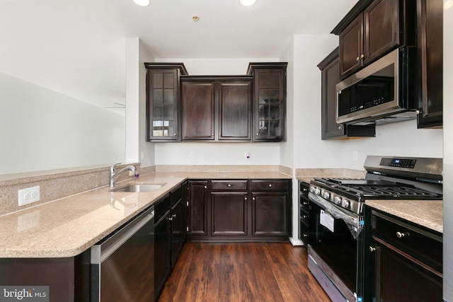 kitchen with light stone counters, appliances with stainless steel finishes, glass insert cabinets, dark wood-type flooring, and a sink