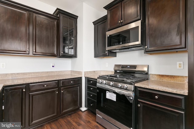 kitchen featuring light stone counters, dark wood finished floors, appliances with stainless steel finishes, glass insert cabinets, and dark brown cabinetry