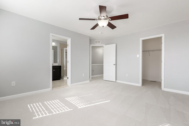 unfurnished bedroom with light colored carpet, visible vents, baseboards, a closet, and a walk in closet