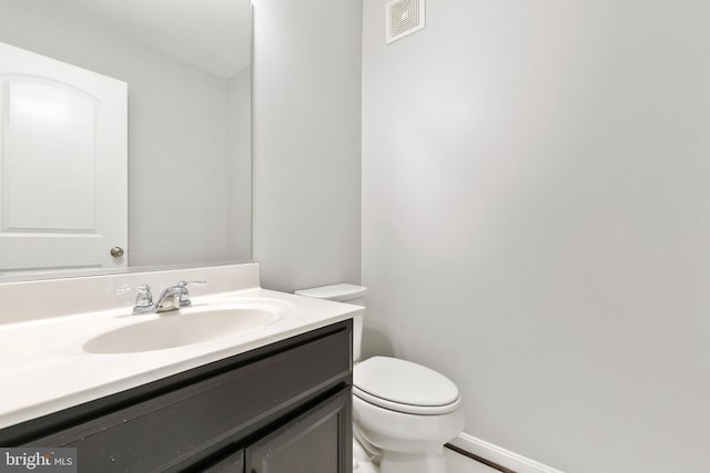 half bath with visible vents, vanity, toilet, and baseboards