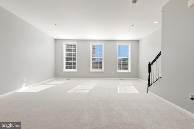 empty room featuring baseboards, stairs, and light colored carpet