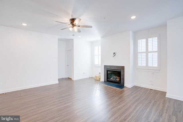 unfurnished living room with wood finished floors, recessed lighting, a fireplace with flush hearth, and baseboards