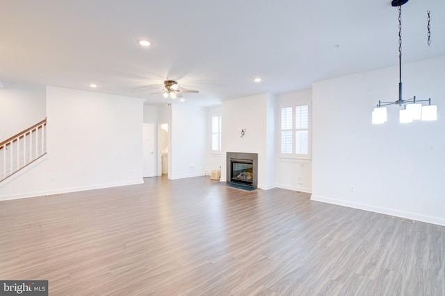 unfurnished living room with a fireplace with flush hearth, light wood-style floors, ceiling fan, baseboards, and stairs