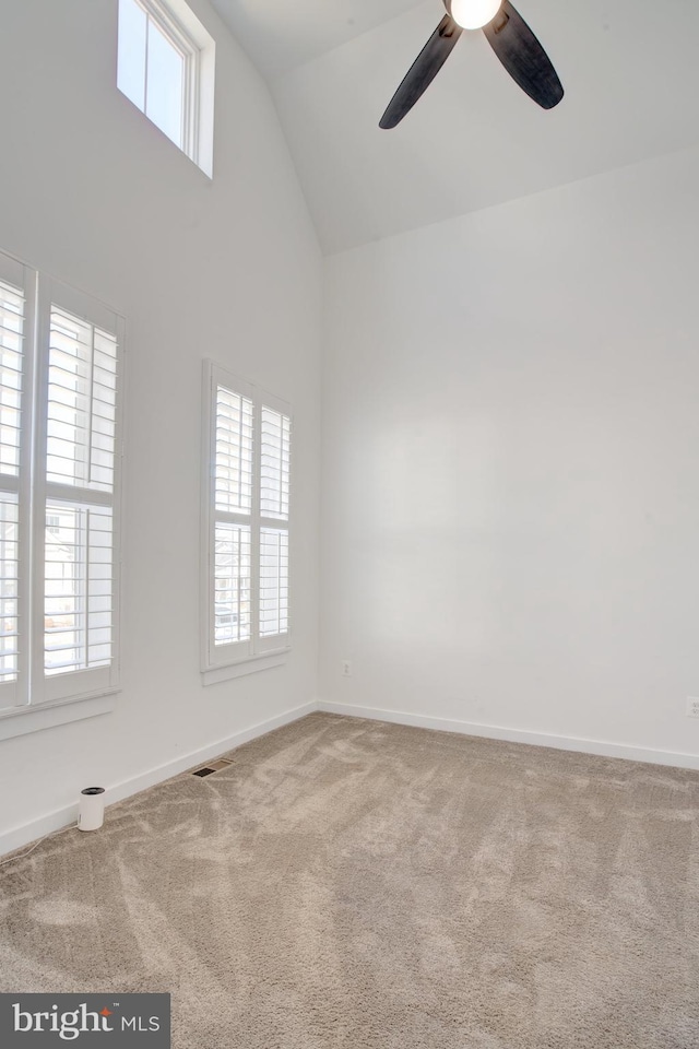 carpeted empty room with ceiling fan, high vaulted ceiling, visible vents, and baseboards