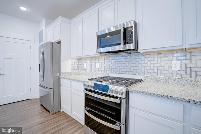 kitchen featuring white cabinets, appliances with stainless steel finishes, light stone counters, light wood-type flooring, and backsplash