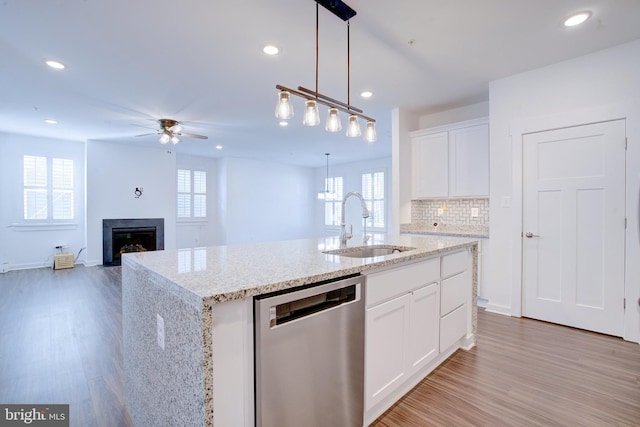 kitchen with decorative light fixtures, white cabinetry, open floor plan, stainless steel dishwasher, and a center island with sink