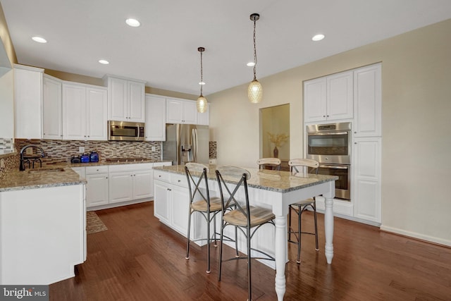 kitchen featuring a kitchen island, appliances with stainless steel finishes, decorative light fixtures, white cabinetry, and sink