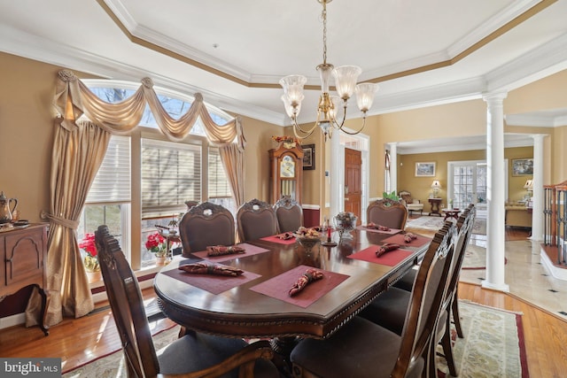 dining room featuring a tray ceiling, ornamental molding, decorative columns, and light hardwood / wood-style flooring