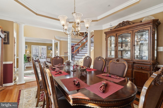 dining space with a notable chandelier, light hardwood / wood-style floors, crown molding, a raised ceiling, and ornate columns