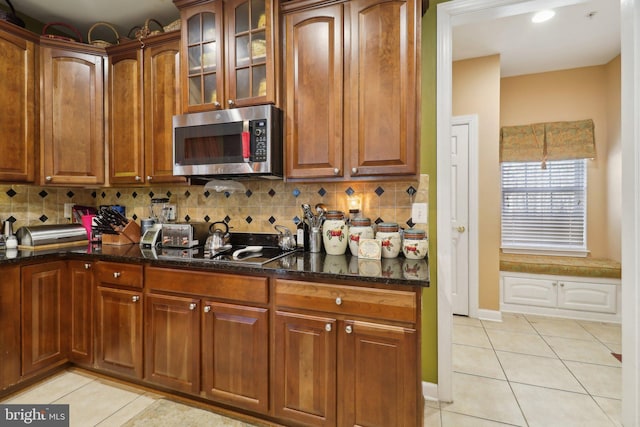 kitchen with dark stone countertops, black cooktop, tasteful backsplash, and light tile patterned floors