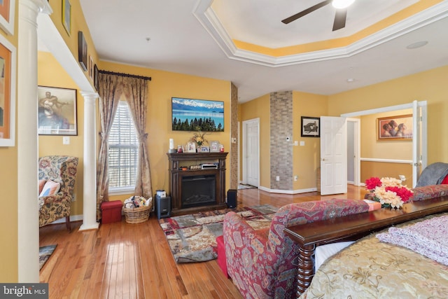 living room featuring hardwood / wood-style flooring, ornate columns, ceiling fan, a raised ceiling, and crown molding