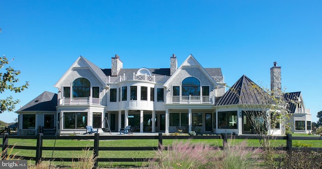 rear view of house with a fenced front yard, a chimney, a lawn, a standing seam roof, and a balcony