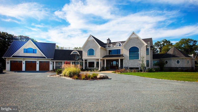 shingle-style home featuring gravel driveway, a front lawn, metal roof, a garage, and a standing seam roof