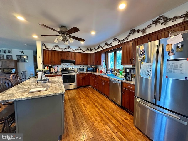 kitchen with a breakfast bar, sink, dark hardwood / wood-style floors, stainless steel appliances, and light stone countertops