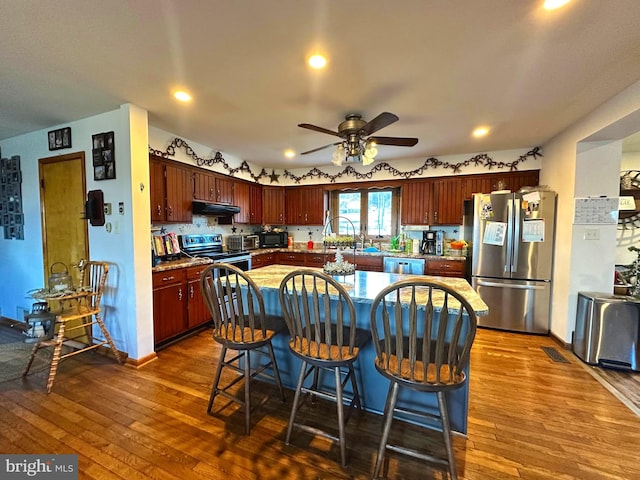 kitchen with a breakfast bar area, tasteful backsplash, appliances with stainless steel finishes, dark hardwood / wood-style flooring, and ceiling fan