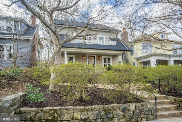 view of front of house featuring covered porch, roof with shingles, a chimney, and stucco siding