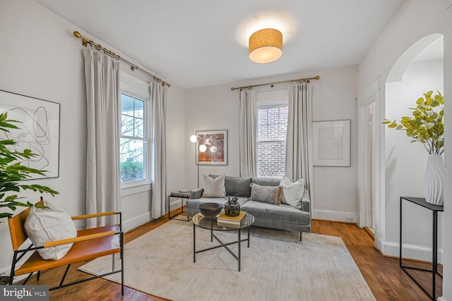 sitting room with arched walkways, baseboards, wood finished floors, and a healthy amount of sunlight