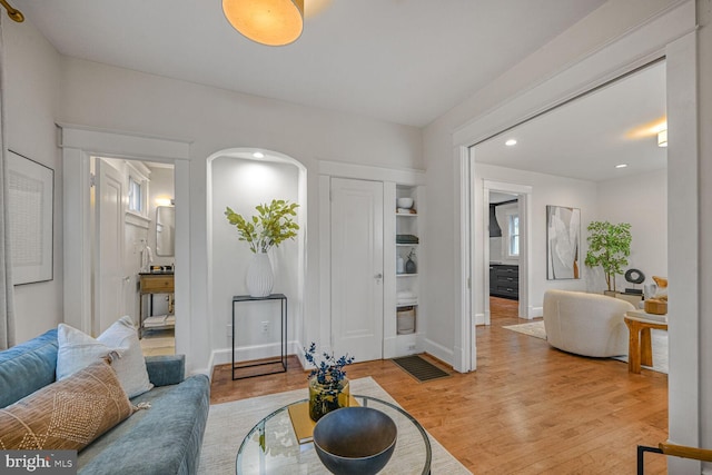 living area with light wood-type flooring, arched walkways, baseboards, and recessed lighting