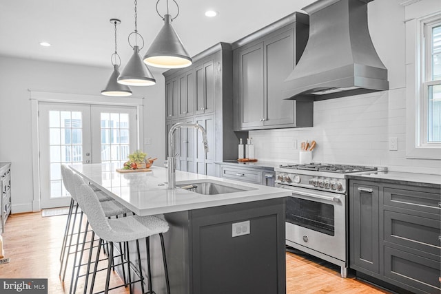 kitchen with light wood-style flooring, a sink, a healthy amount of sunlight, wall chimney range hood, and high end stainless steel range oven