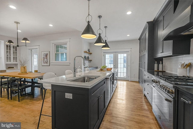 kitchen with stainless steel appliances, a sink, wall chimney range hood, light wood-type flooring, and backsplash