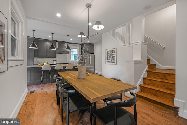 dining space featuring light wood-style flooring, visible vents, stairway, and baseboards