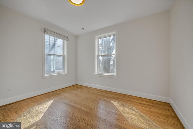 spare room with a healthy amount of sunlight, visible vents, baseboards, and wood finished floors