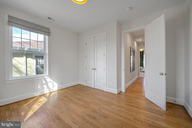 unfurnished bedroom with a closet, light wood-type flooring, visible vents, and baseboards