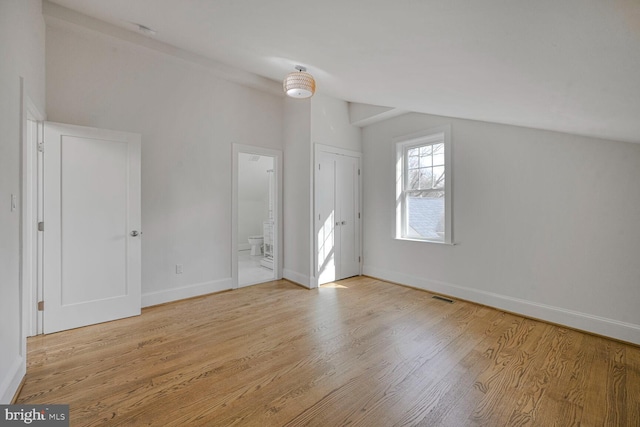 interior space with baseboards, visible vents, connected bathroom, wood finished floors, and vaulted ceiling