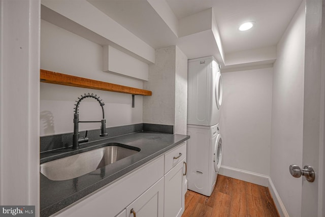 washroom with stacked washer and dryer, cabinet space, a sink, light wood-type flooring, and baseboards