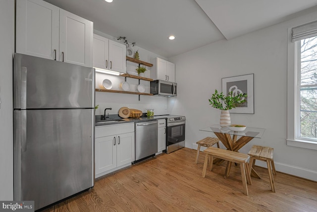 kitchen with open shelves, light wood-style flooring, appliances with stainless steel finishes, white cabinetry, and a sink