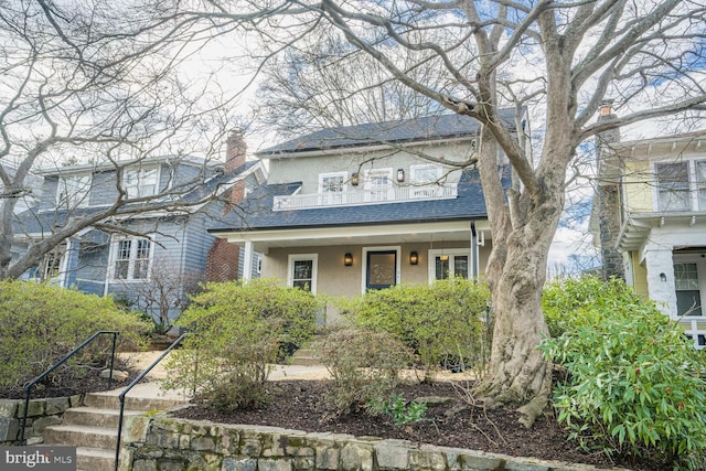 view of front of house with a shingled roof, covered porch, a chimney, and stucco siding