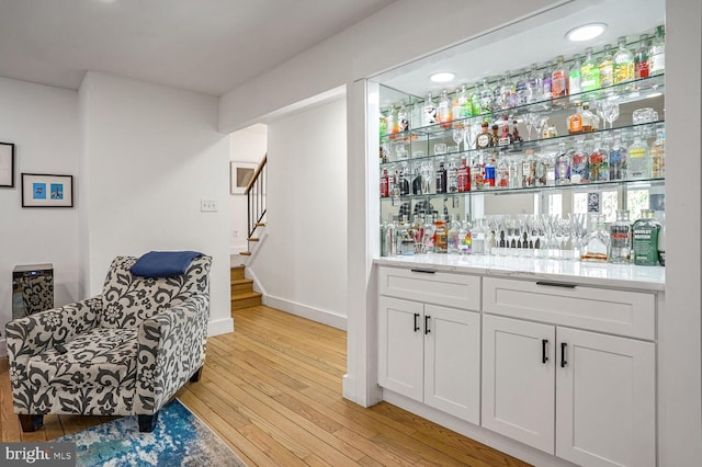 bar with white cabinetry, light stone counters, and light wood-type flooring