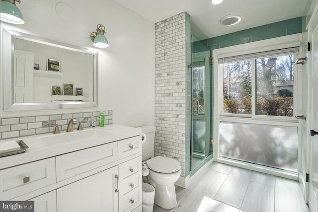 bathroom with a shower with door, toilet, vanity, and decorative backsplash