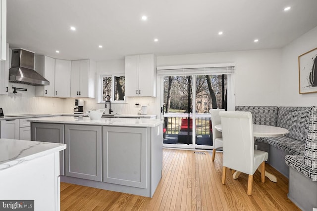 kitchen featuring gray cabinetry, tasteful backsplash, a center island, light stone countertops, and wall chimney range hood