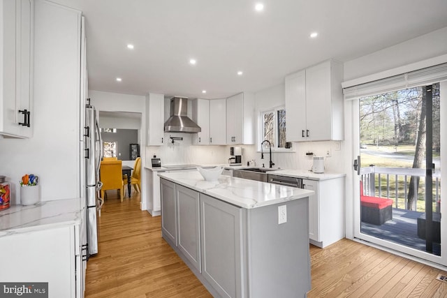 kitchen featuring white cabinetry, a center island, light hardwood / wood-style floors, light stone countertops, and wall chimney range hood