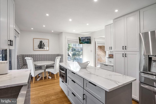 kitchen with a kitchen island, white cabinets, stainless steel fridge, light hardwood / wood-style floors, and light stone countertops