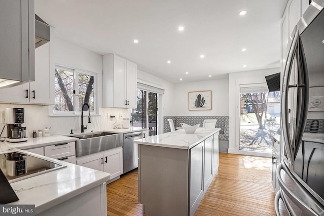 kitchen featuring sink, a center island, appliances with stainless steel finishes, light stone countertops, and white cabinets