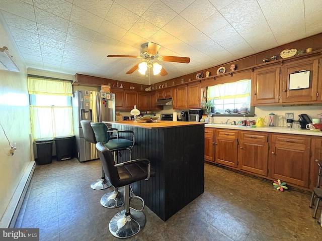 kitchen with stainless steel refrigerator with ice dispenser, sink, a breakfast bar area, a baseboard radiator, and ceiling fan