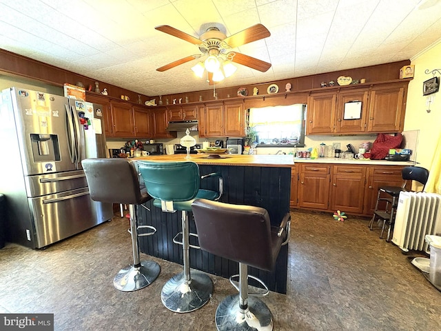 kitchen with ceiling fan, a kitchen island, a kitchen bar, wood counters, and stainless steel fridge with ice dispenser