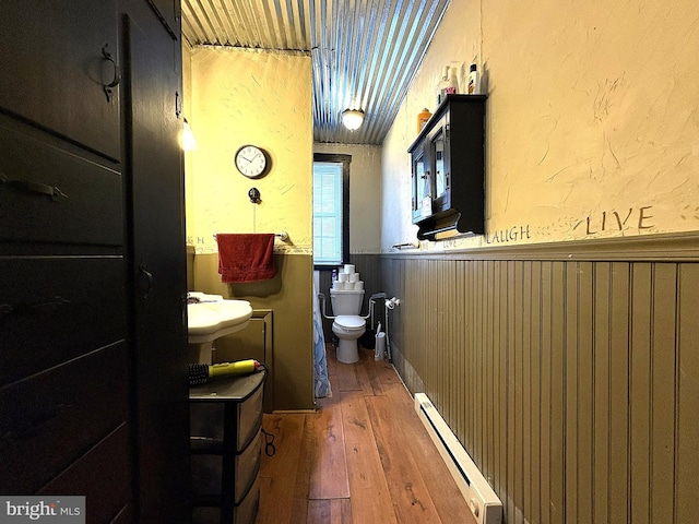 bathroom with hardwood / wood-style flooring, baseboard heating, and toilet