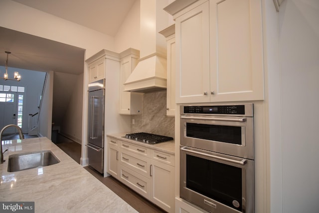 kitchen with light stone counters, appliances with stainless steel finishes, sink, and custom exhaust hood