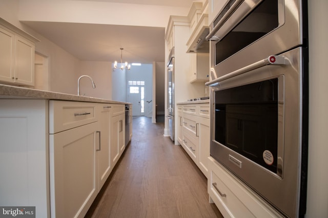 kitchen featuring pendant lighting, wood-type flooring, white cabinets, an inviting chandelier, and wall chimney exhaust hood