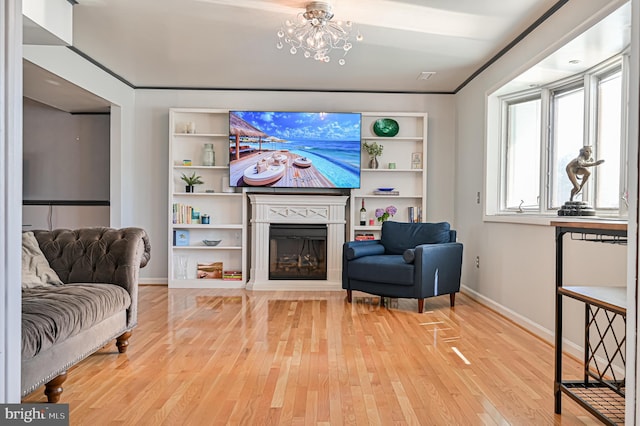 sitting room featuring built in shelves, ornamental molding, wood-type flooring, and a chandelier