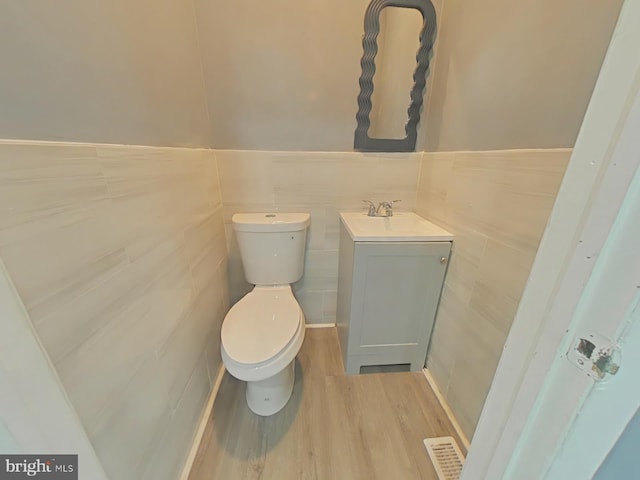 bathroom with hardwood / wood-style flooring, vanity, toilet, and tile walls